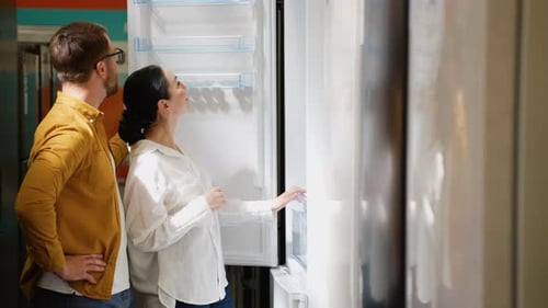 Young Couple Chooses a Fridge in a Consumer Electronics Store for New Home