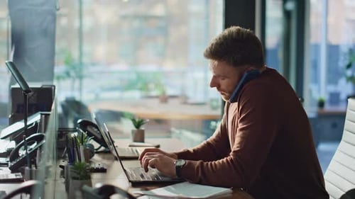 Man Working at Desk on Laptop and Phone