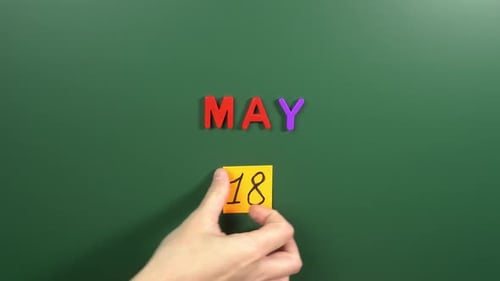 Hand sticking a sticker 18 May calendar day on school board. 18 date of May. Eighteenth day May