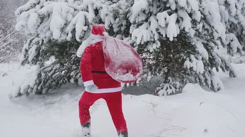Père Noël avec un grand sac rouge de cadeaux marchant en hiver dans la forêt enneigée Un père Noël drôle se dépêche