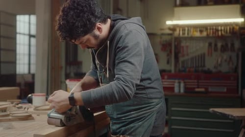 Man Smooths Wood with Tool in Workshop