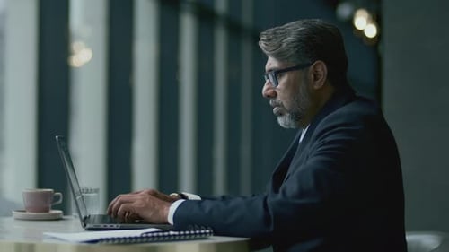 Mid-Aged Businessman in Formal Attire Using Laptop at Restaurant Table