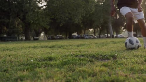 A teenager plays soccer in a field at sunset