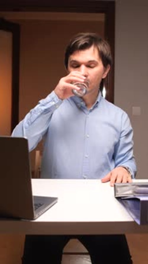 Vídeo vertical: Empleado de oficina tomando medicamentos en el trabajo con un ordenador portátil y archivos