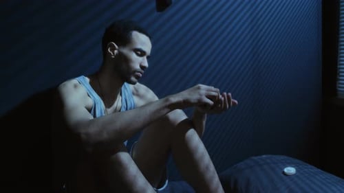 Man Sitting on Bed Handling Pills at Night