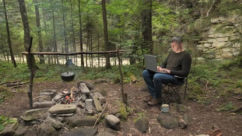 A Man Works on a Laptop in a Tourist Camp in a Beautiful Forest