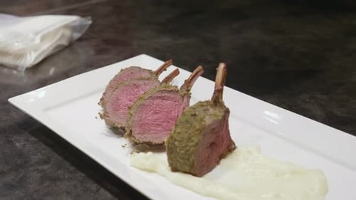 Venison meat ribs slices, with green spice on top, plated on a white plate with mashed potato. Clos