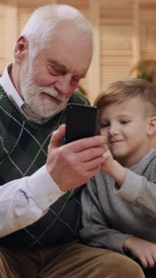 Grandfather and Grandson Look at Phone Indoors