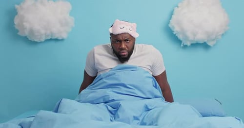 Man in Bed with Sleep Mask Looking Annoyed