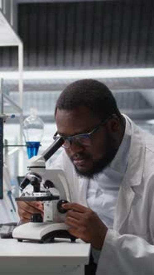 Scientist Uses Microscope in Lab with Colleague