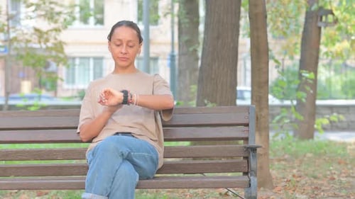 Woman Checking Smartwatch on Bench in Urban Park