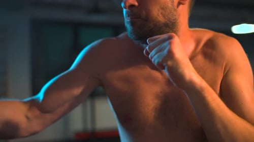 Alone Boxer is Working Out Blows on a Punching Bag in a Gym in Evening