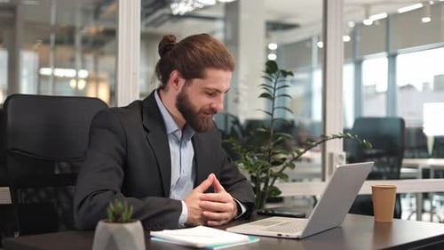 Bearded Male Manager Having Online Call Using Portable Computer in Office
