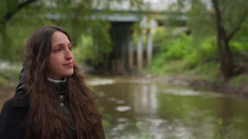 Caucasian Female Gazing Thoughtfully at Flowing Water Beneath Bridge Young Woman with Long Brown