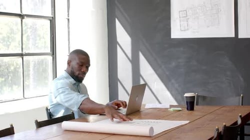 Architect working on blueprints and using laptop in modern office
