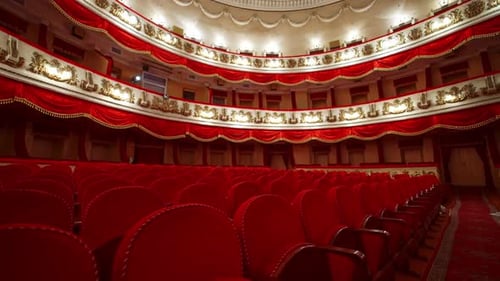 Panoramic view of beautiful richly decorated theater hall. Rows of red chairs in theater hall.