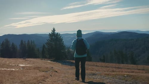Female with backpack hiking in mountains. Woman walking on dirt trail on hike