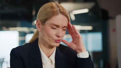 Exhausted Stressed Overworked Businesswoman Experiencing a Headache in Office