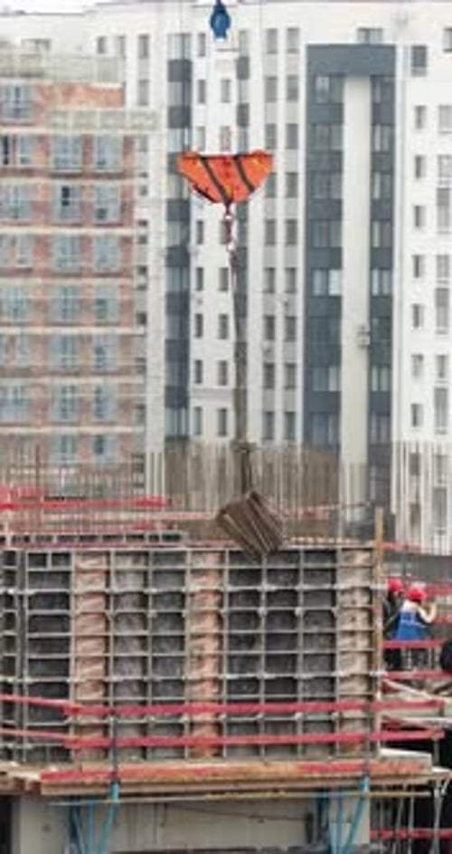 Vertical Aerial Drone Dynamic Orbit Around Crane Load Lowering Rebar to Construction Workers