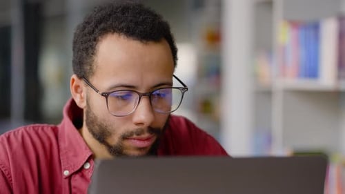 Steadicam Shot Multiethnic Serious Man Teacher Freelance Coach Wearing Glasses Works on Laptop