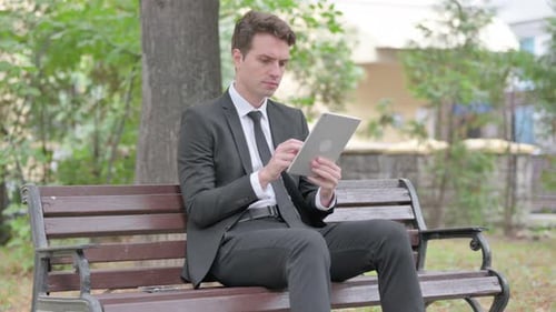 Young Businessman using Tablet while Sitting Outdoor on a Bench
