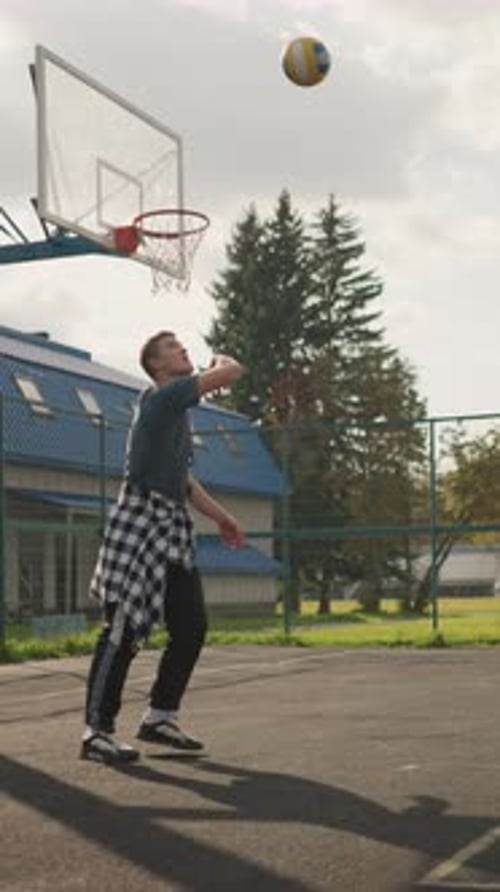 Man Preparing to Slam Volleyball in Outdoor Court with Background Featuring Basketball Hoop