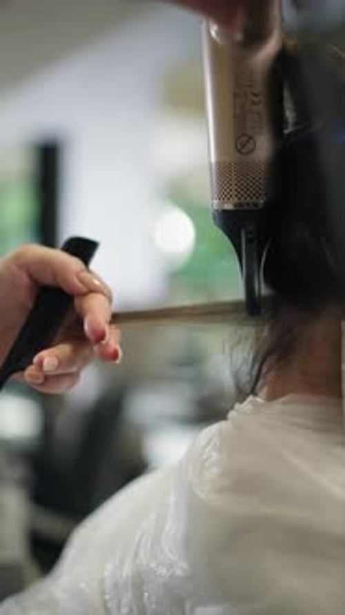 Hairdresser styling client's hair with dryer in salon