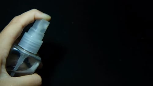 female hand with spray bottle cleaning close up on black background. Hand Sanitizer