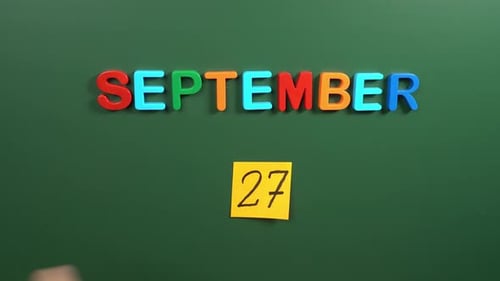 Hand sticking a sticker 27 September calendar day on school board. 27 date of September. Twenty