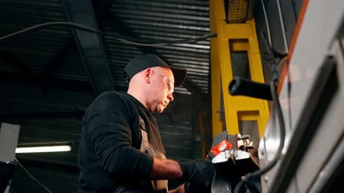Low Shot Car Mechanic Working at a Service Station with an Angle Grinder From Which Sparks Fly