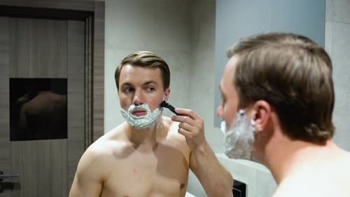 Man Shaving His Beard in Bathroom Mirror