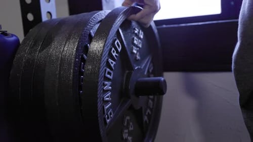 Weightlifter adding heavy 45lb steel plate to powerlifting bar for strength training