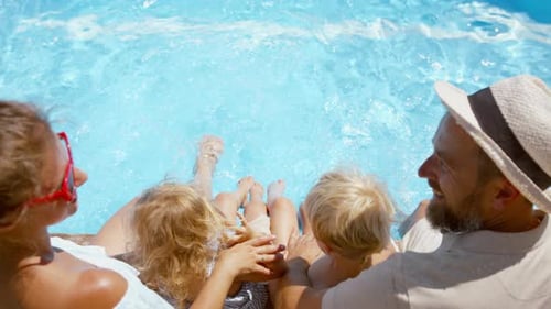 Top View Of Beautiful Family Sitting On The Edge Of The Pool And Having Fun Together.