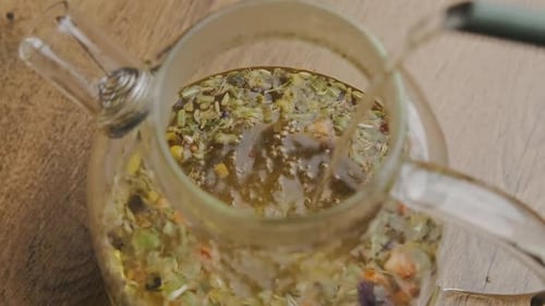Pouring Herbal Tea into Glass Teapot on Wood