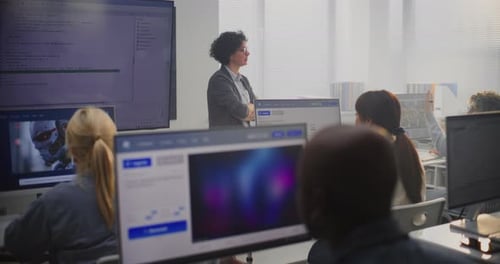 Lehrerin steht neben einem großen Bildschirm, auf dem Programmcode angezeigt wird, der Modellierungskonzepte erklärt