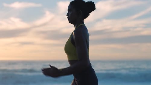 Fast, fit and active woman running by the ocean and beach shore with sunset sky background