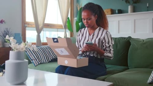 Woman Opens Package and Uses Mobile Phone Indoors