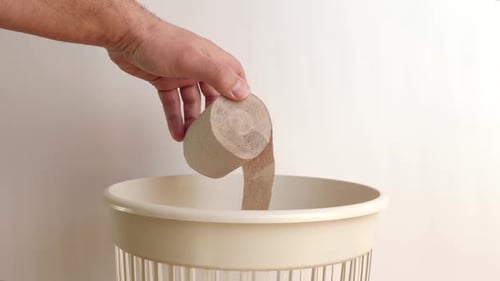 Hand Discards Empty Toilet Paper Roll in Trash