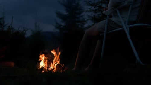 Lit night fire close-up rest of a tourist sits on an armchair against backdrop of fire and mountains