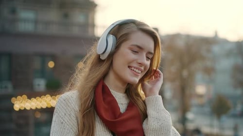 Smiling girl listens to favorite song on headphones walking down city street