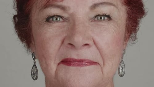 Close-up studio portrait of an attractive senior woman with red hair and elegant earrings giving a p