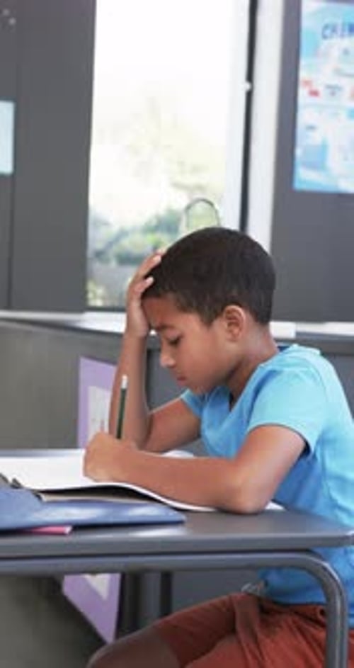 Vertical video: In school, child studying and writing in notebook, concentrating on work