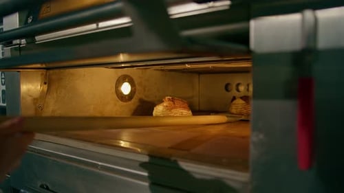 female baker takes out freshly baked fresh bread from the oven and puts it on shelf in the kitchen