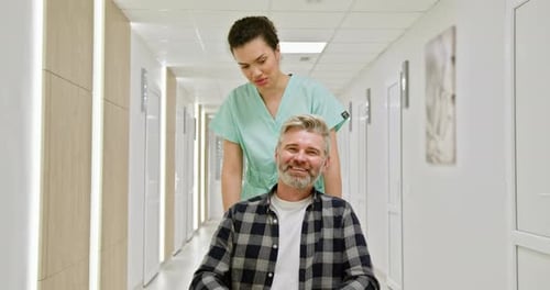 Nurse Assisting Elderly Man in Wheelchair Through Hospital Hallway A Nurse