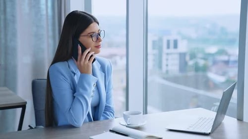 Beautiful brunette lady sitting at desk in the office having phone conversation.