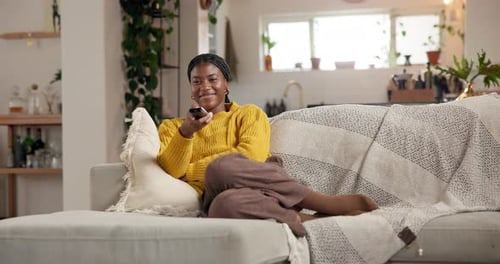 Woman Relaxes on Sofa with Remote in Sunlit Interior