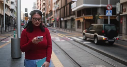 Woman Using Smartphone with Headphones on City Street