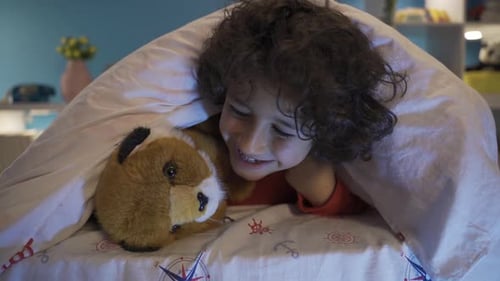 Cute boy hiding under the bed with his toy dog, playing.