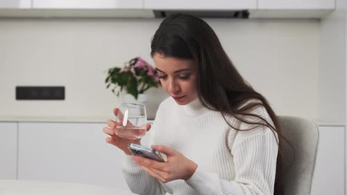 Woman Using Phone and Drinking Water at Home