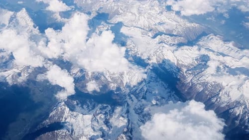 aerial view snow covered mountain peaks scattered white clouds dramatic shadows across terrain high